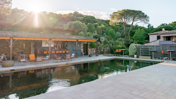 A poolside area with outdoor seating and a bar, surrounded by lush greenery and trees. - Bastide de Ramatuelle (Ramatuelle)
