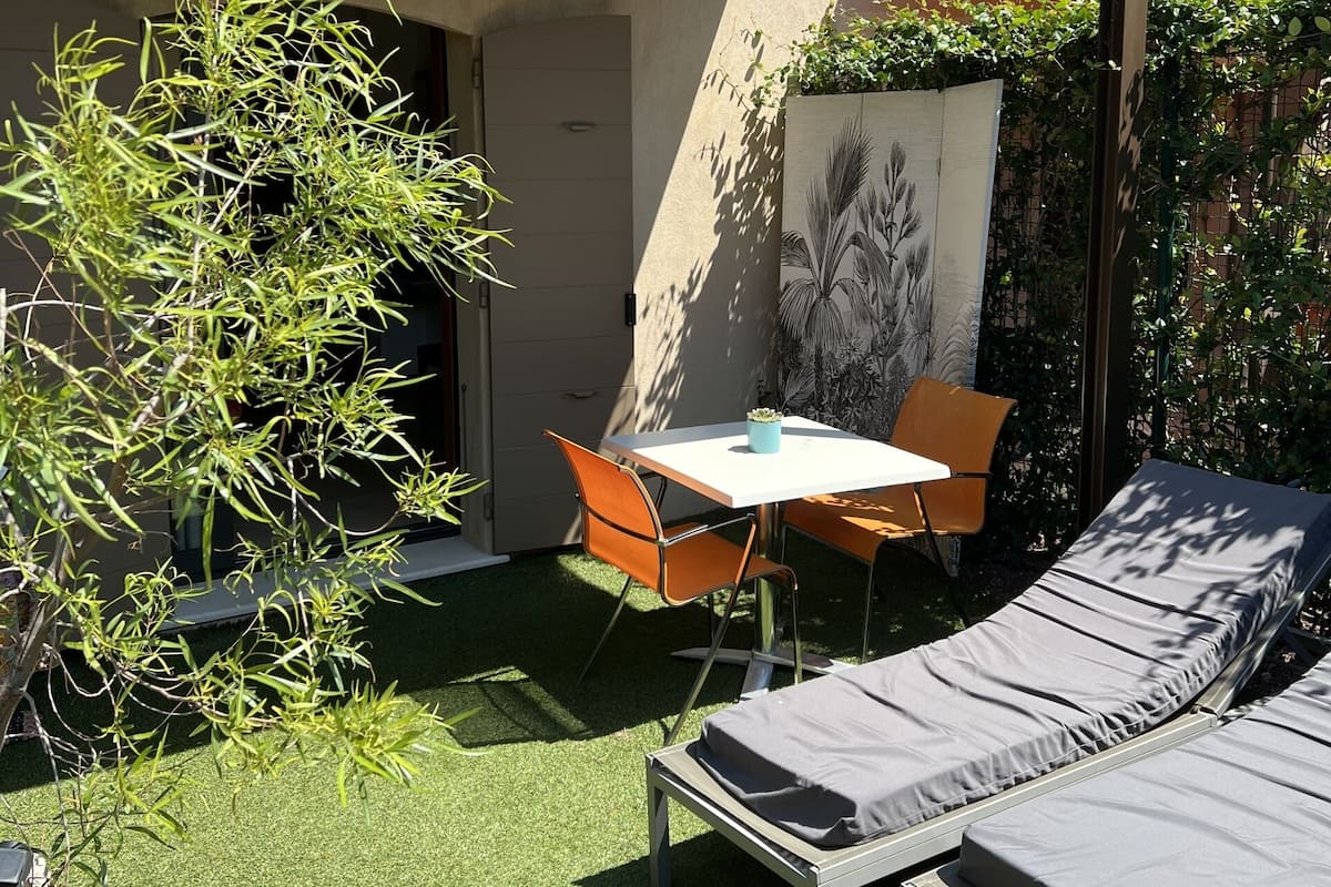 A modern outdoor patio with artificial grass, a table, two lounge chairs, and a potted plant.