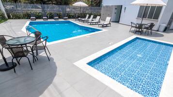 A swimming pool area with two pools, lounge chairs, and tables.
