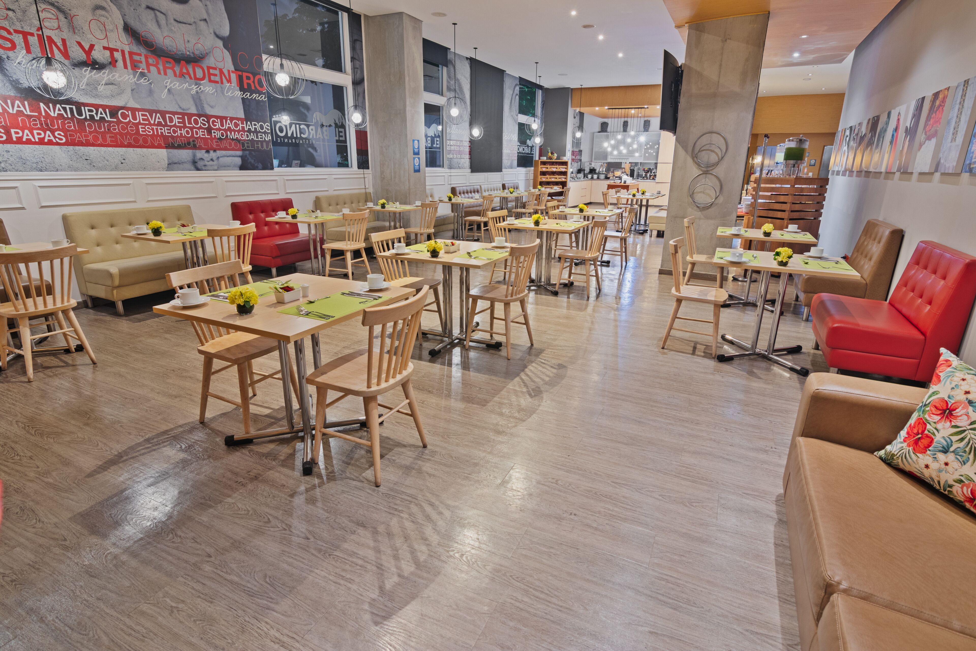 A spacious restaurant with wooden tables and chairs, red cushioned seating, and a large mural on the wall.