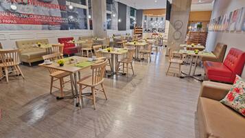 A spacious restaurant with wooden tables and chairs, red cushioned seating, and a large mural on the wall.