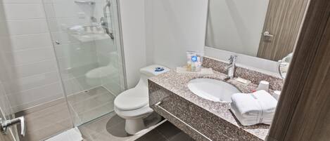 Un baño moderno con cabina de ducha de vidrio, inodoro blanco, lavamanos con encimera de granito y un espejo grande.