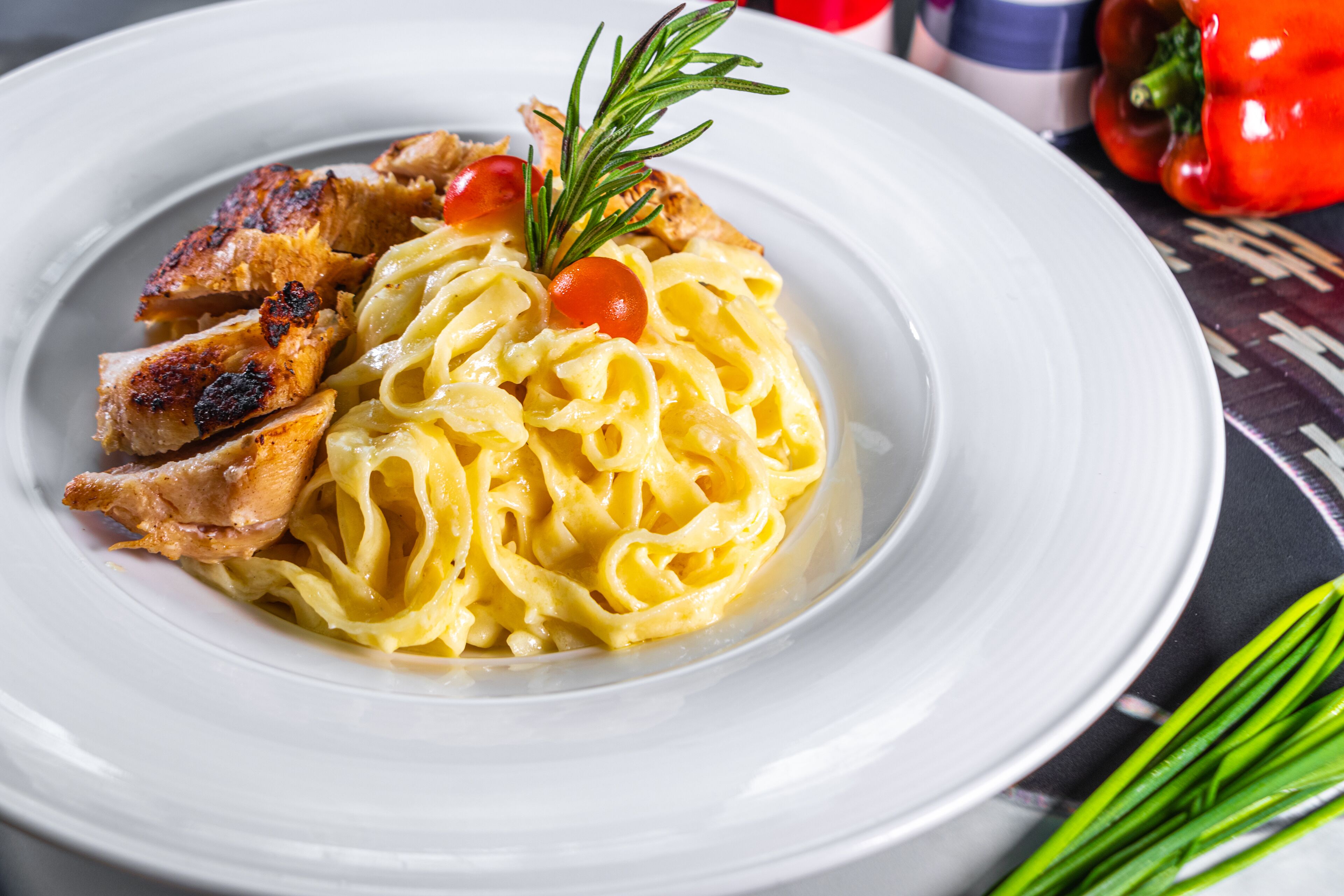 A plate of pasta with grilled chicken and a garnish of rosemary and cherry tomatoes.