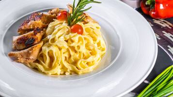 Un plato de pasta con pollo a la parrilla y un adorno de romero y tomates cherry.