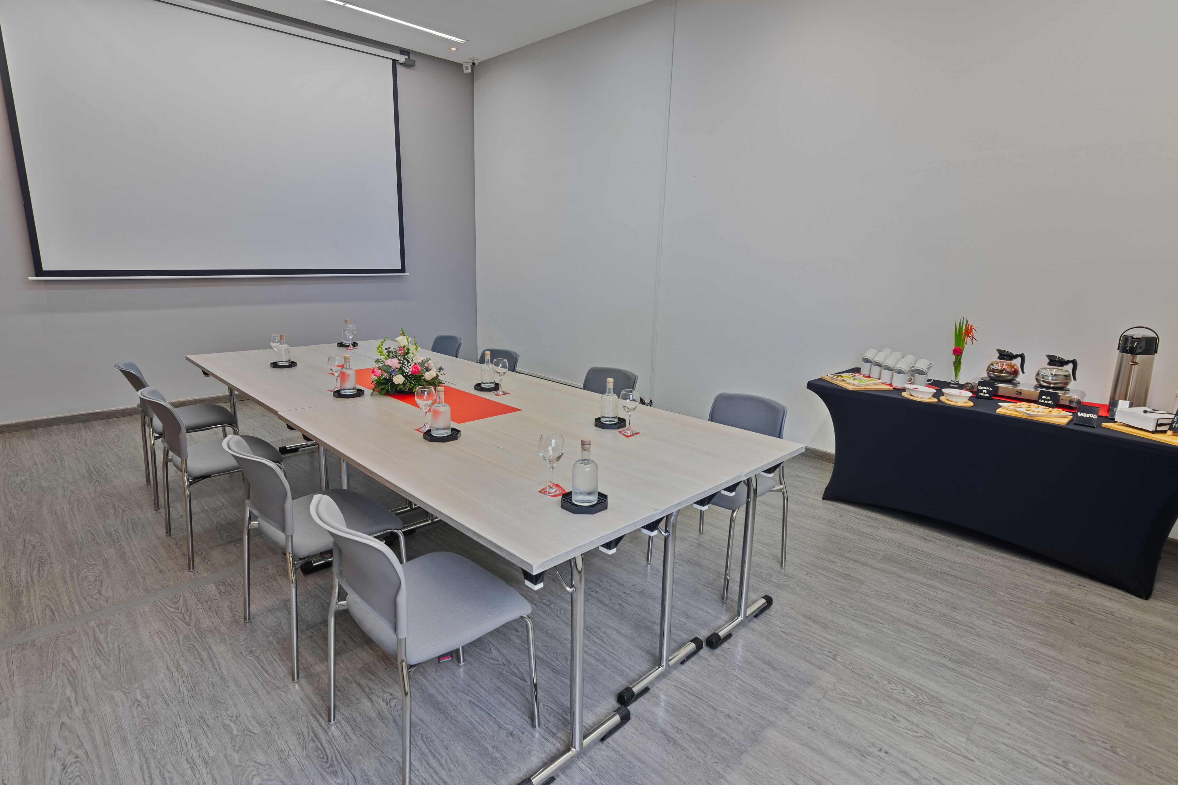 A conference room with a long table, chairs, a projector screen, and a buffet table with food and drinks.