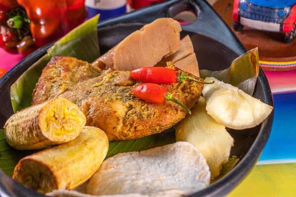A variety of food items including a fish, plantains, and a banana, served on a banana leaf.