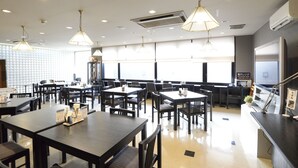 Un restaurante espacioso con varias mesas y sillas, luces de techo y amplios ventanales.