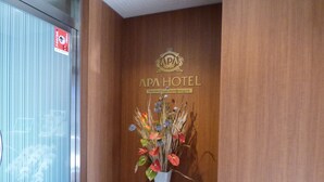 Un área de recepción con una pared de madera, un letrero de APA HOTEL y un jarrón con flores.