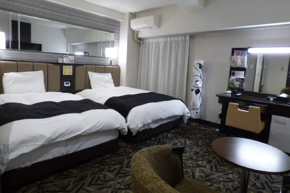 A hotel room with two beds, a desk, a chair, and a small table.