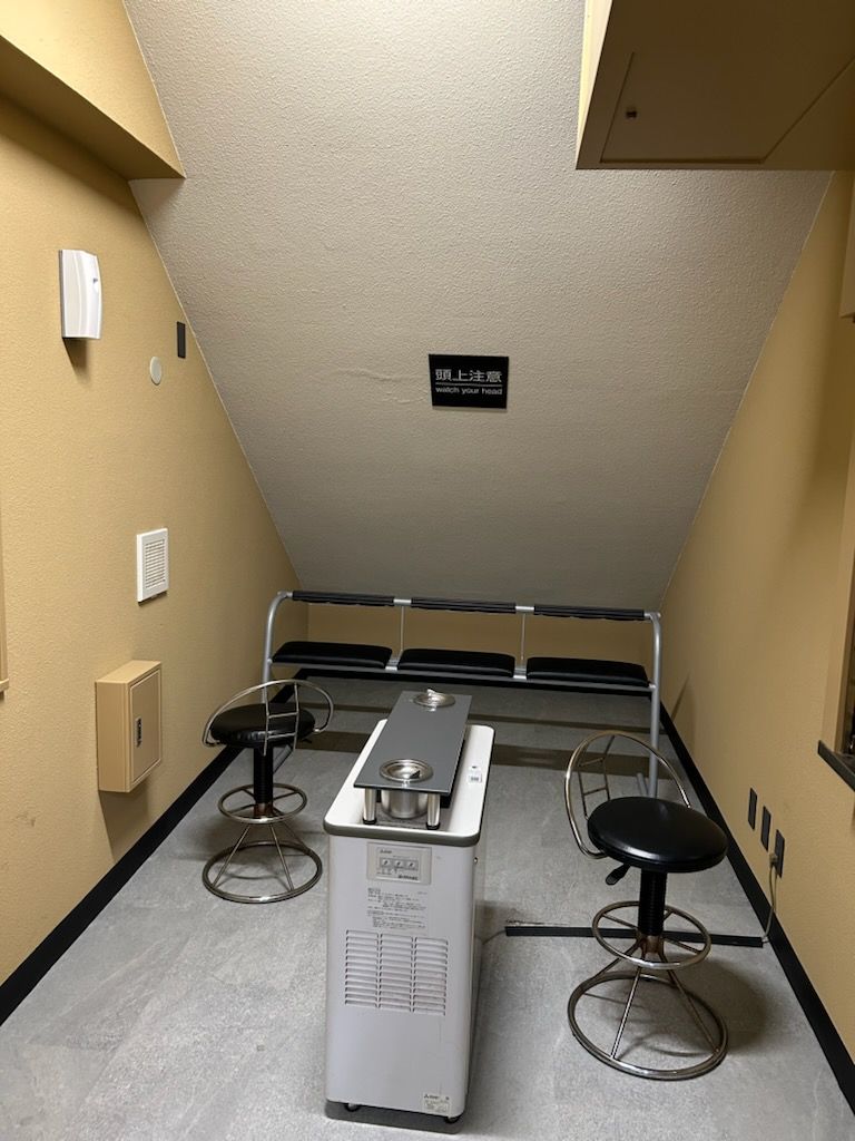 A small kitchenette with a stove, two bar stools, and a ceiling-mounted vent.