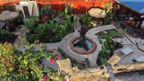 A hotel with a green roof, outdoor seating, a central water feature, and a variety of tropical plants. - Poshtel Arenal (La Fortuna)