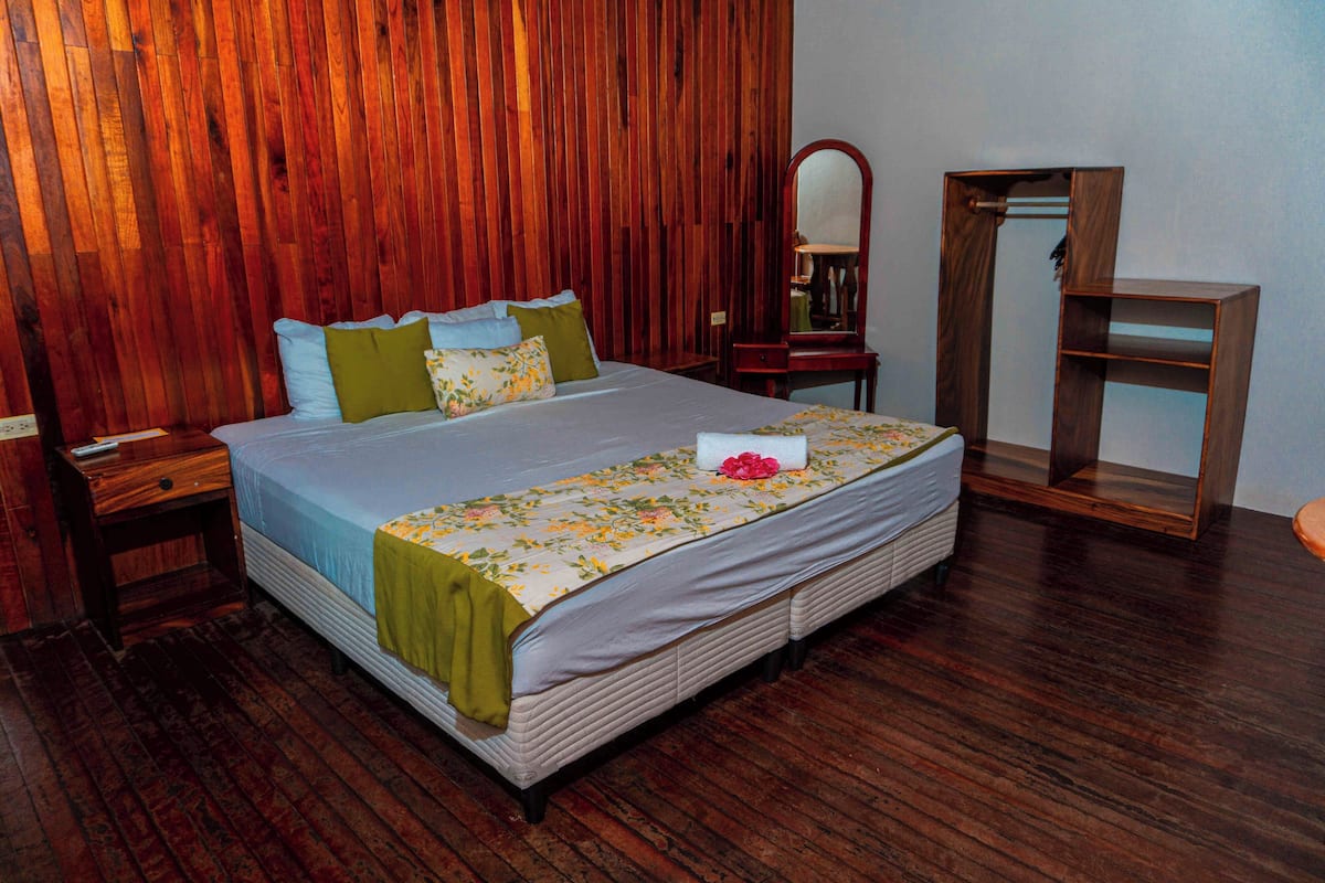 A bedroom with a wooden headboard, a bed with multiple pillows, a bedside table, a mirror, and a wooden nightstand.