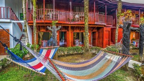 A wooden building with balconies, a hammock, and tropical plants. - Poshtel Arenal (La Fortuna)