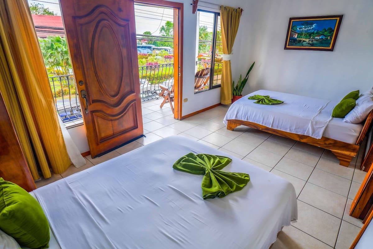 A hotel room with two beds, a balcony with a view of the garden, and a painting on the wall.