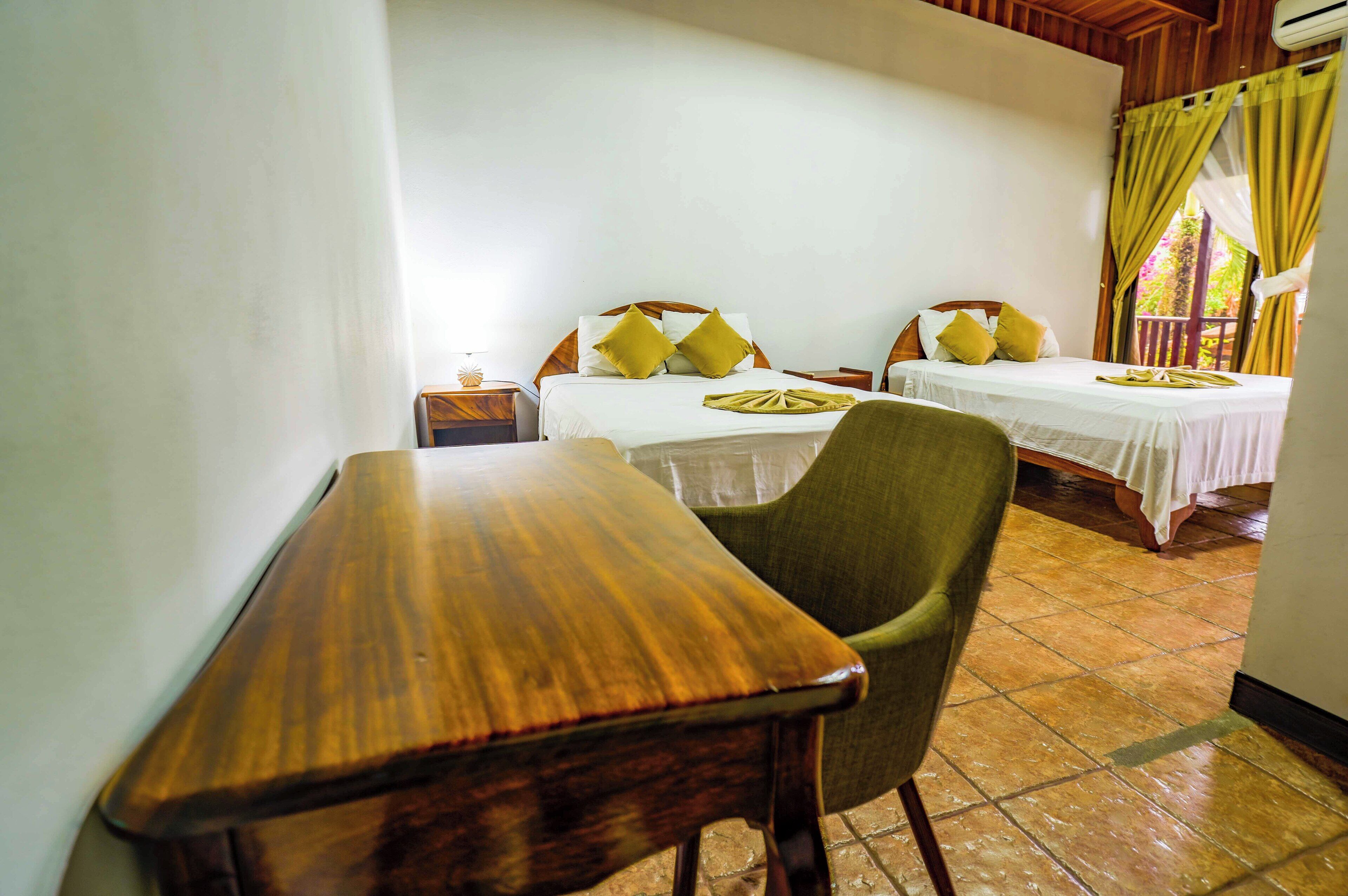 Quarto com duas camas, uma mesa de madeira e uma cadeira verde.