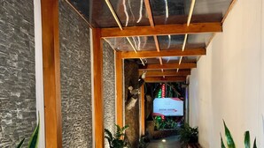 A corridor with wooden beams, stone walls, and potted plants. - Poshtel Arenal (La Fortuna)