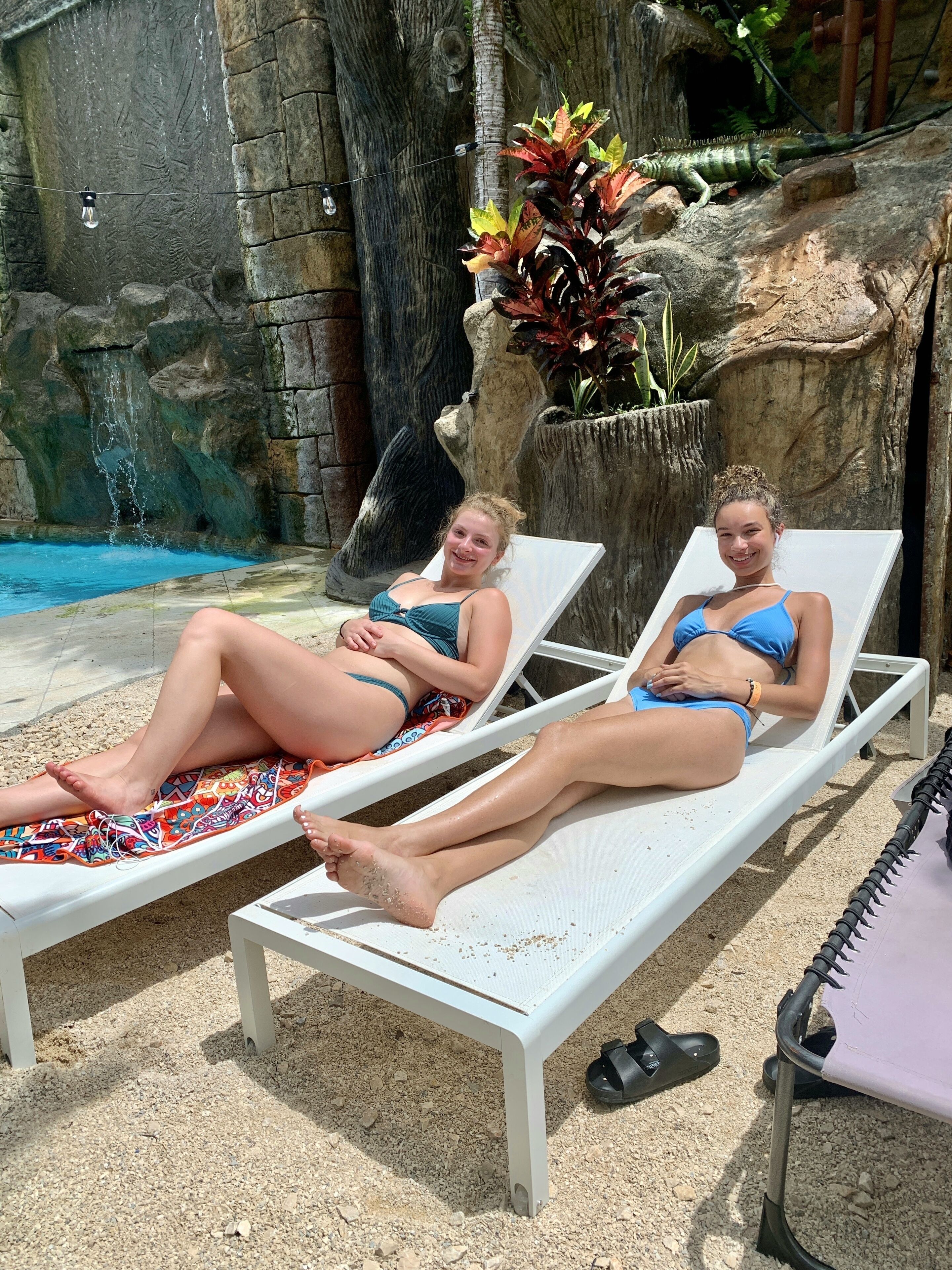 Two lounge chairs by a pool with a rocky backdrop and a waterfall feature.