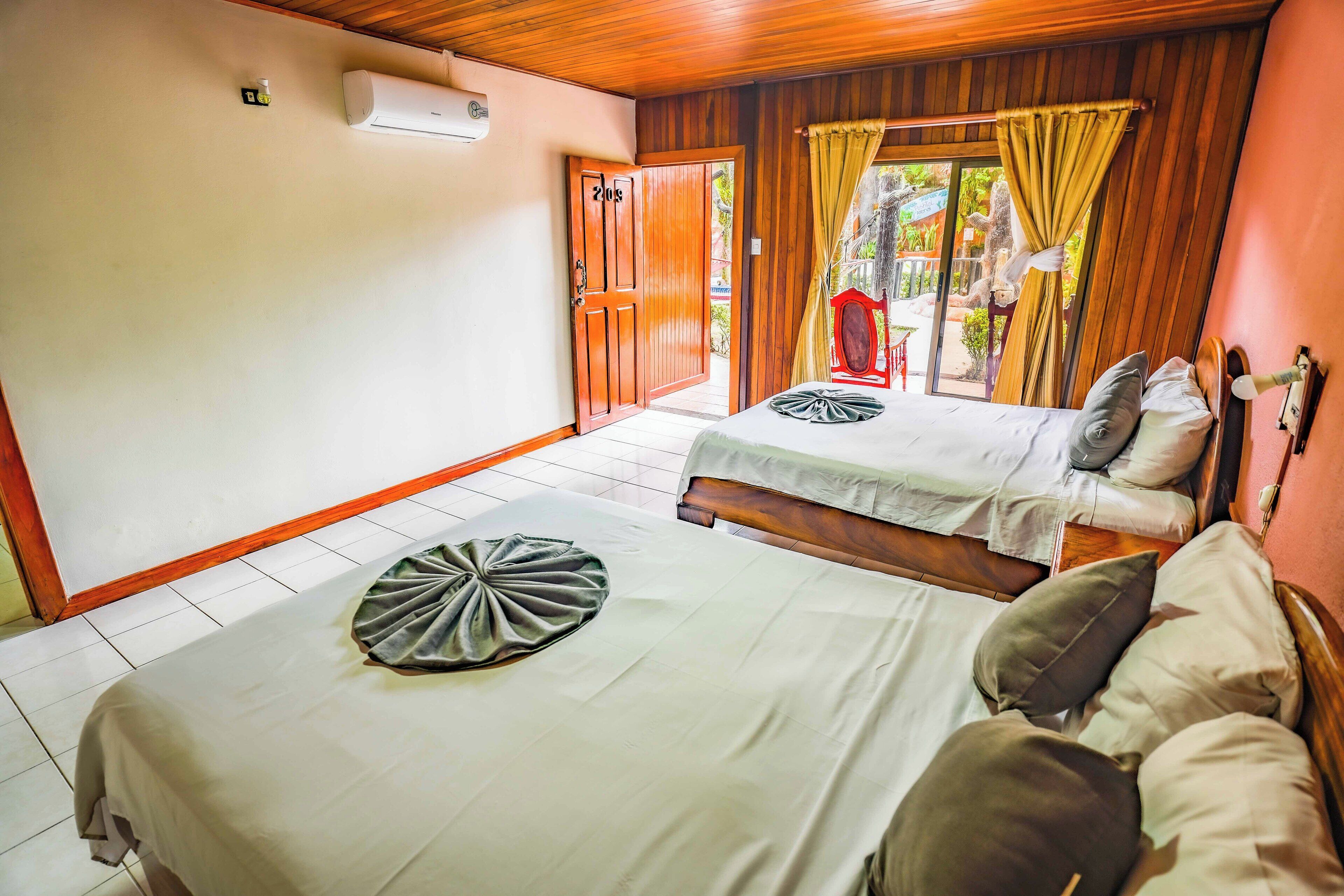 A room with two beds, a wooden ceiling, and a sliding door leading to an outdoor area.