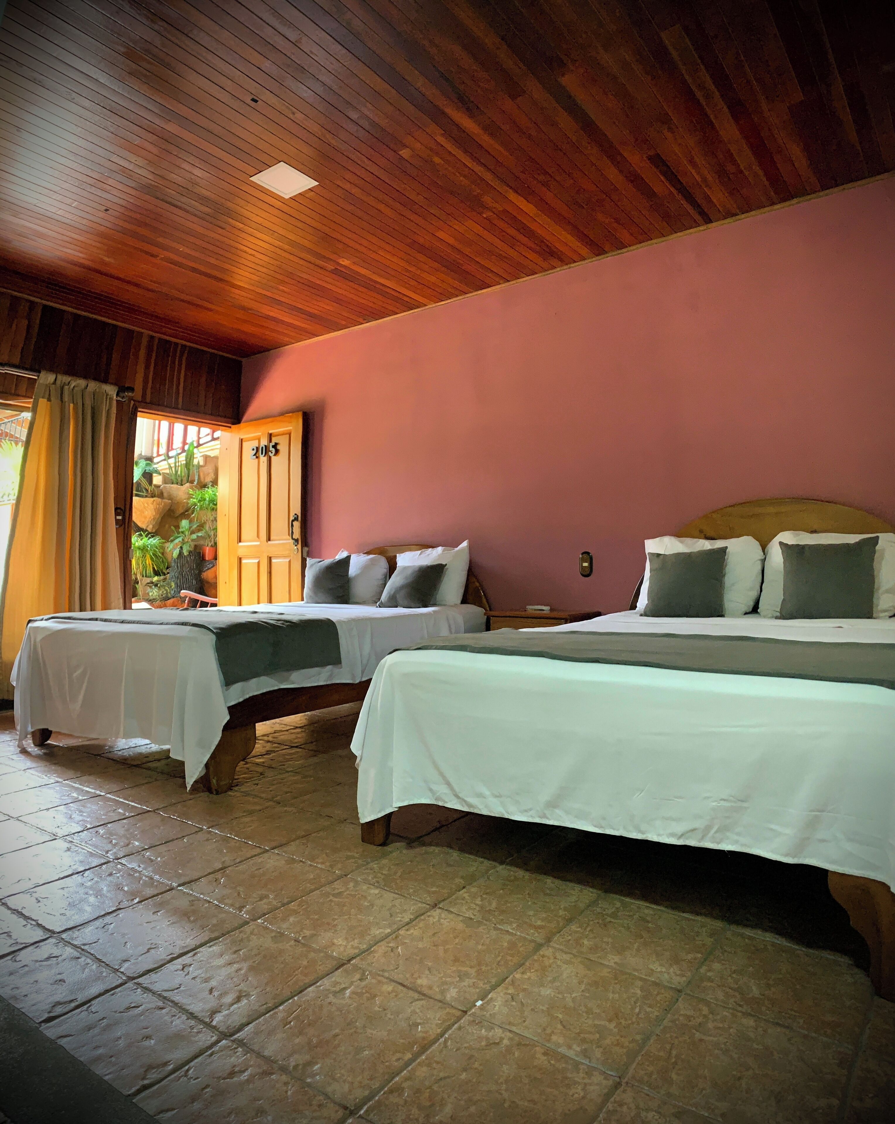 A room with two beds, wooden ceiling, and a door with the number 205.