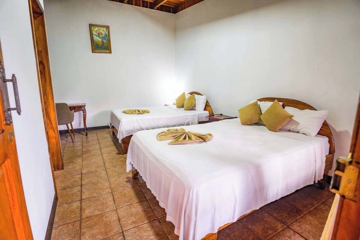A hotel room with two beds, each with white linens and pillows, a small table, and a chair.