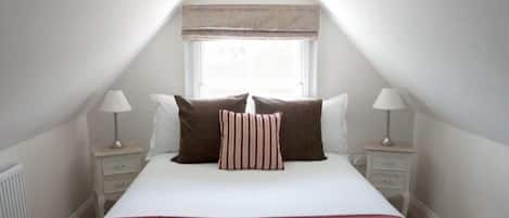 A bedroom with a large bed, two bedside tables with lamps, a window with a wooden valance, and a radiator.