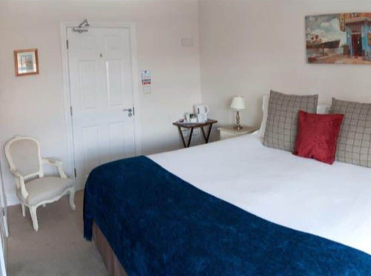 A hotel room with a bed, a chair, a small table with a lamp, and a painting on the wall.