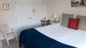 A hotel room with a bed, a chair, a small table with a lamp, and a painting on the wall.