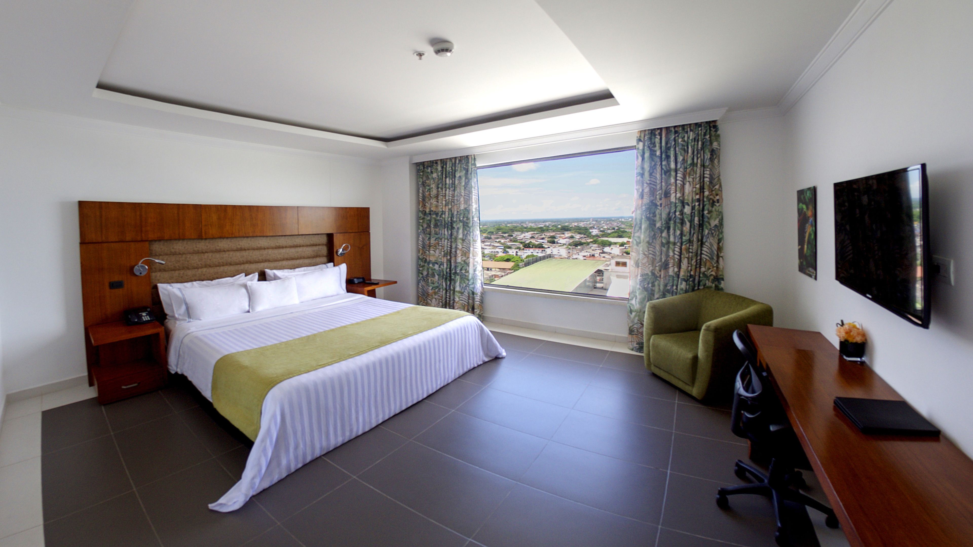 A hotel room with a large bed, a desk, a chair, and a TV.