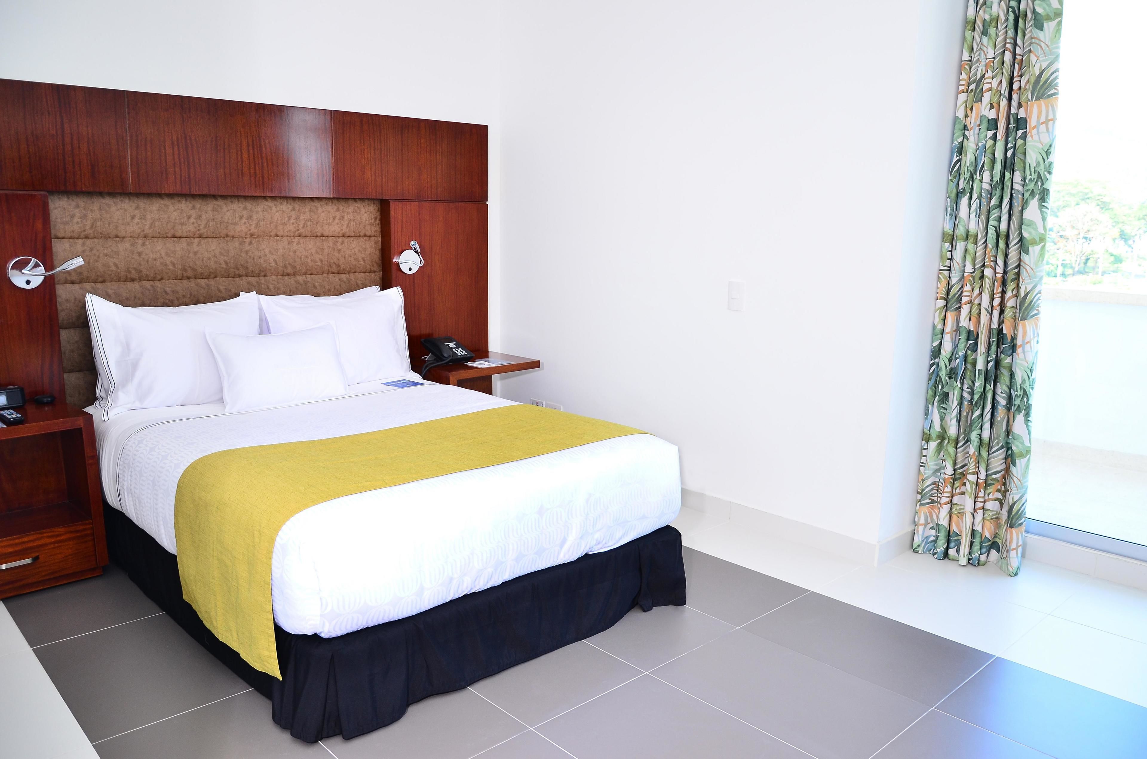 A hotel room with a large bed, wooden headboard, bedside tables with lamps, and a window with curtains.