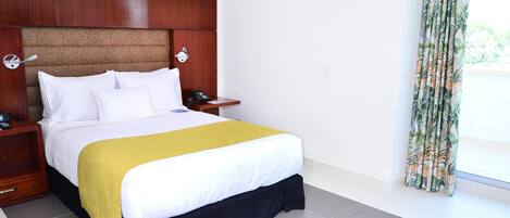 A hotel room with a large bed, wooden headboard, bedside tables with lamps, and a window with curtains.