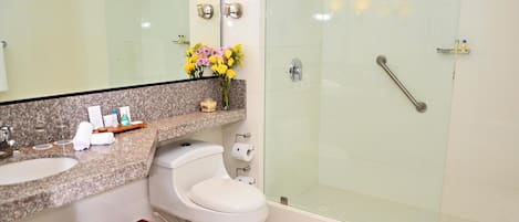 Un baño moderno con encimera de granito, inodoro blanco, cabina de ducha de vidrio y espejo sobre el lavabo.