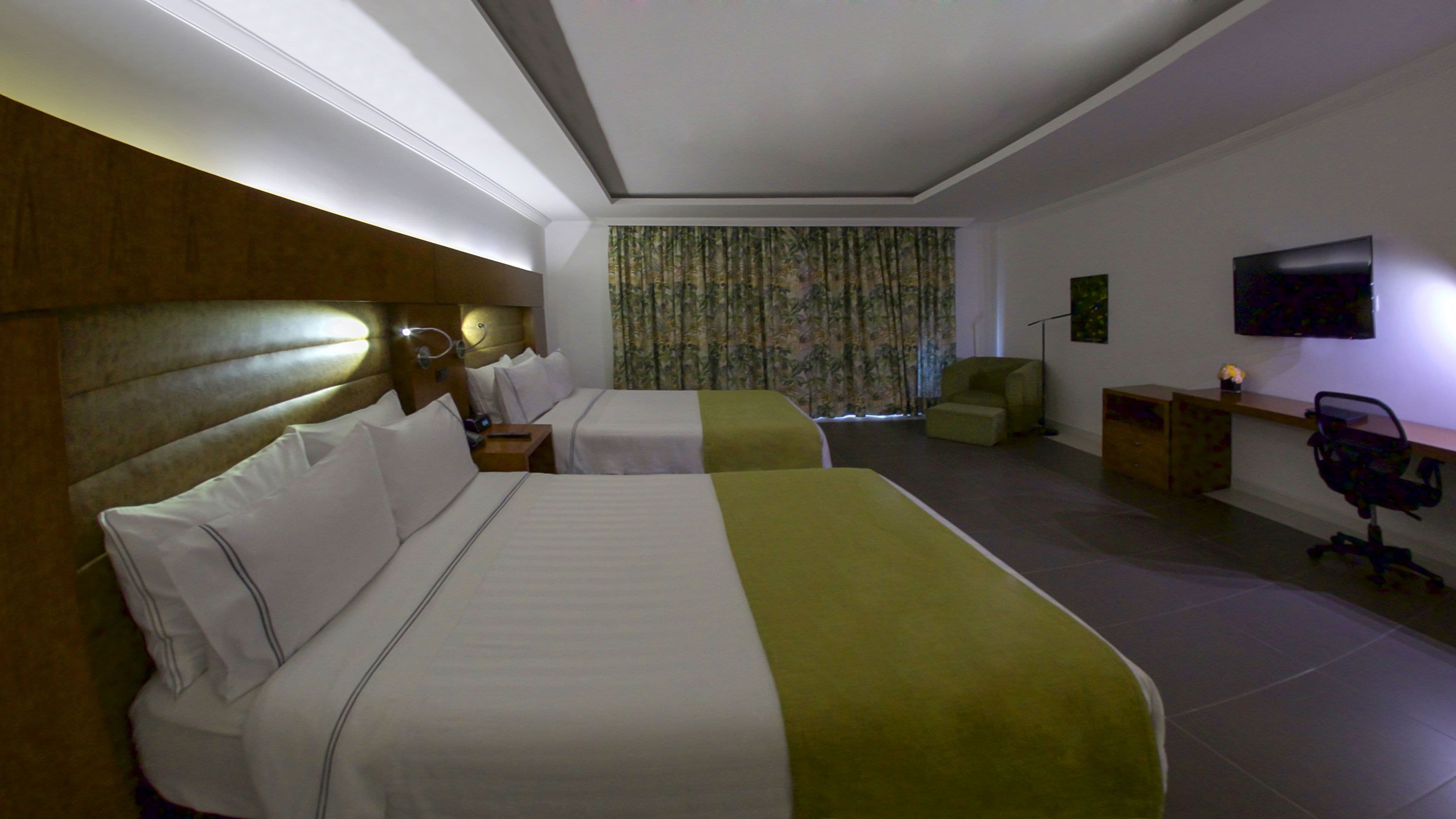 Een hotelkamer met twee bedden, een bureau, een stoel, een televisie en een raam met gordijnen.
