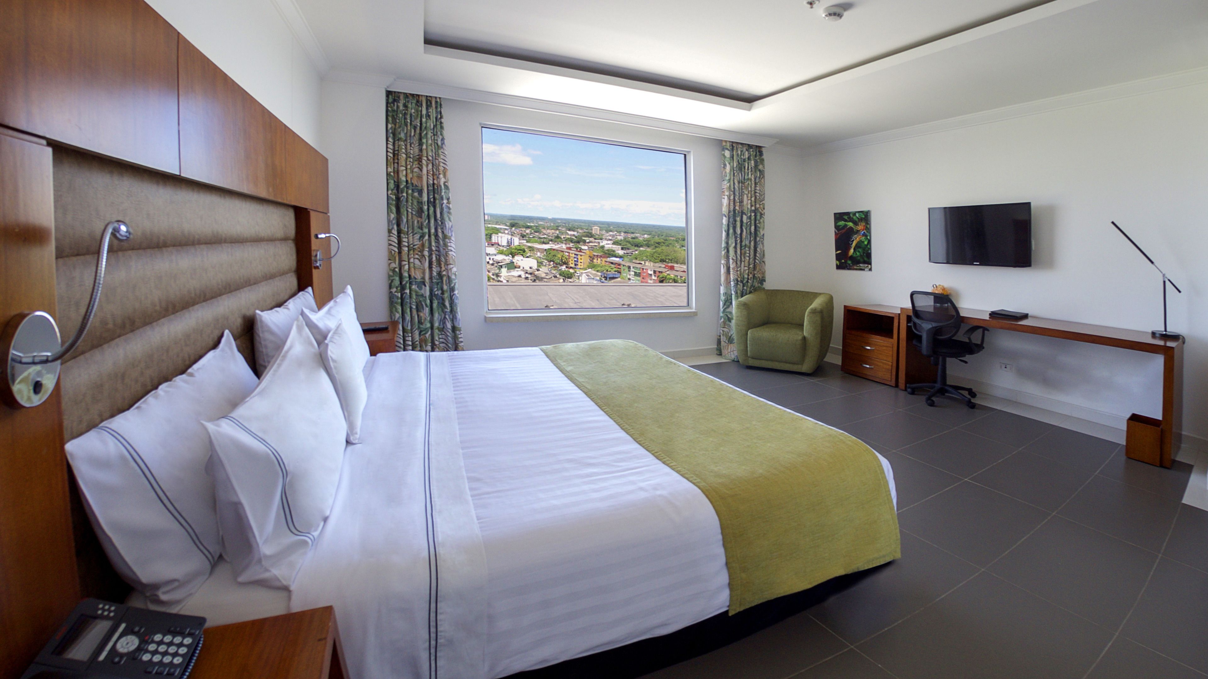 Une chambre d’hôtel avec un grand lit, un bureau, une chaise, une télévision et une vue sur le paysage urbain.