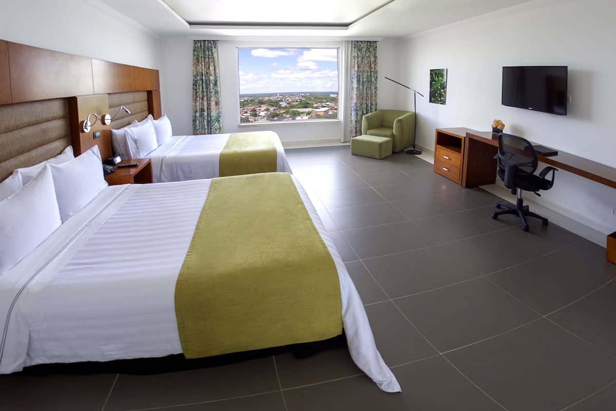 Une chambre d’hôtel avec deux lits, un bureau, une chaise, une télévision et une vue sur la ville.
