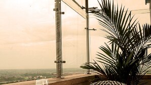 Une table de petit-déjeuner dressée avec une variété de plats et de boissons, une vue sur le paysage urbain et une grande plante en arrière-plan.