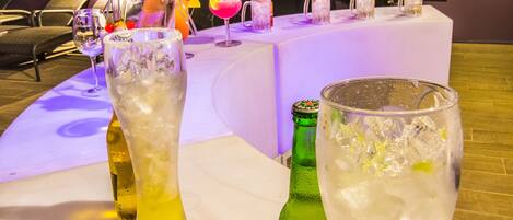 A table with drinks and bottles, a bar area, and a city view at night.