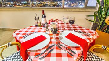 A table set for two with a red and white checkered tablecloth, wine glasses, and a bottle of wine.
