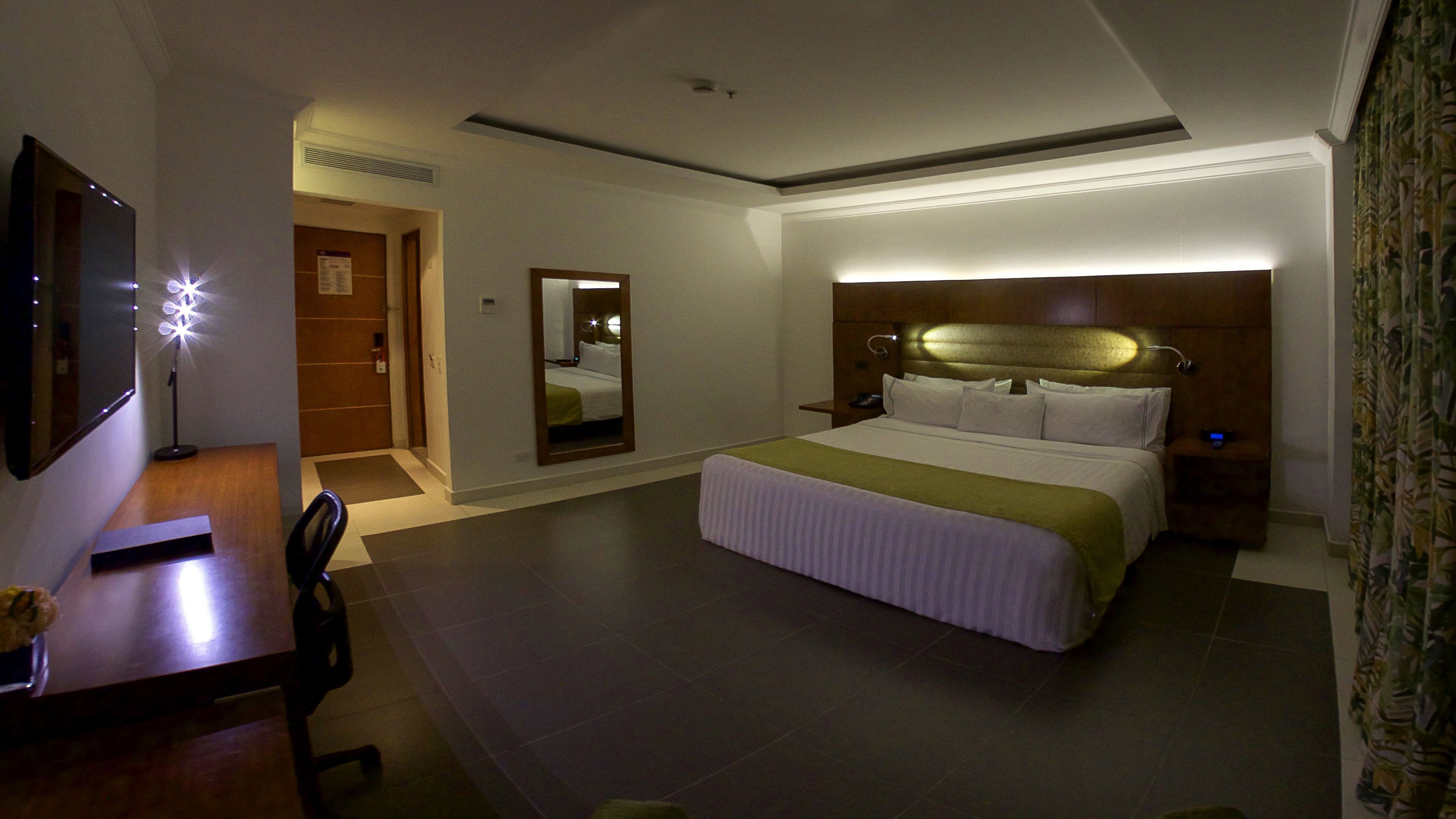 A hotel room with a bed, bedside table, chair, desk, and a mirror.