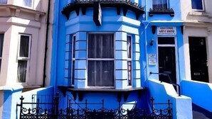 Un edificio en esquina con una fachada azul distintiva, un mirador saliente y una reja metálica negra.