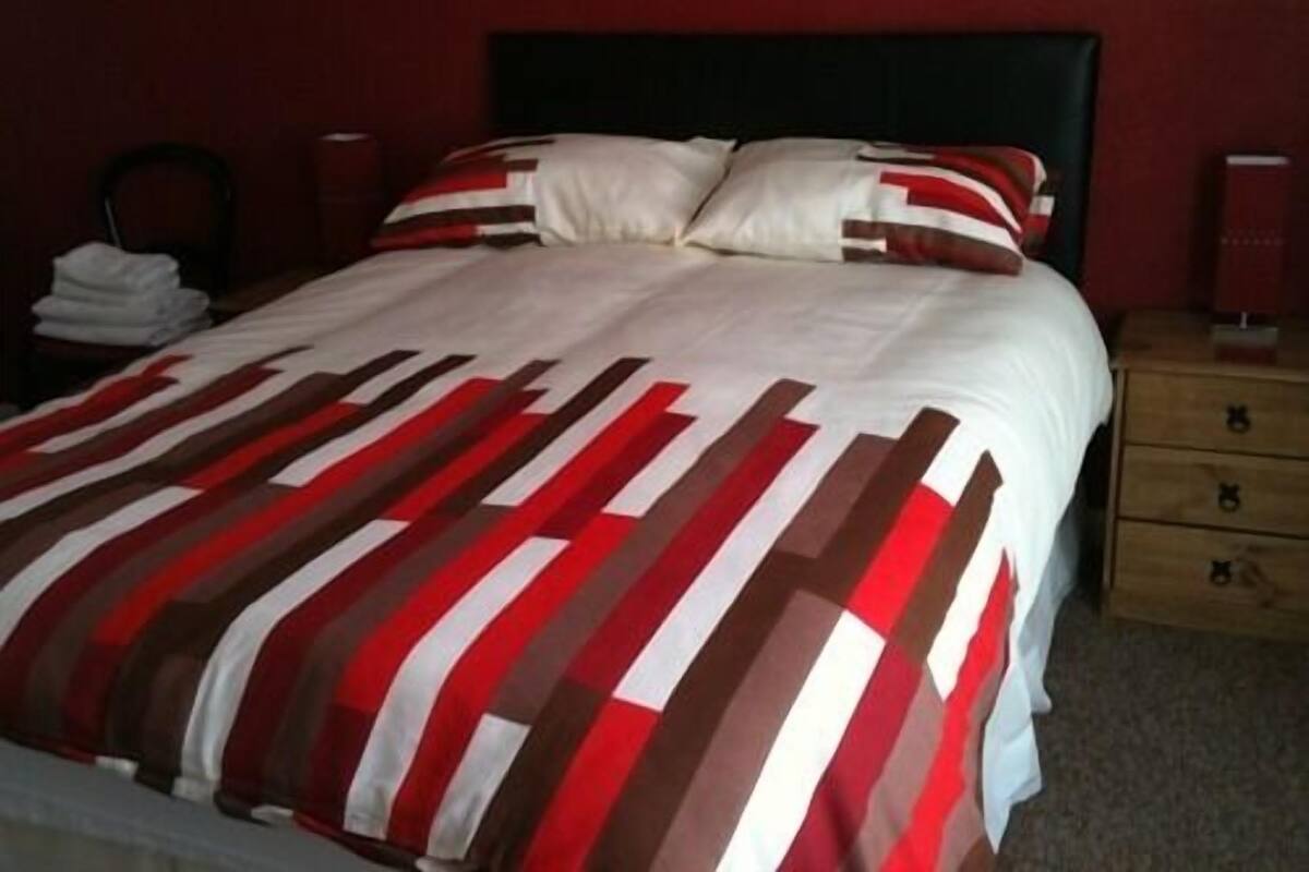 A bed with a striped bedspread, a wooden nightstand with drawers, and a red wall.