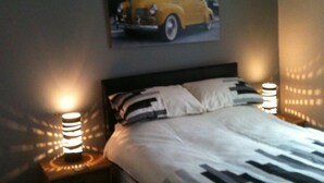Un dormitorio con una cama, dos lámparas de noche y un cartel de un coche amarillo en la pared.