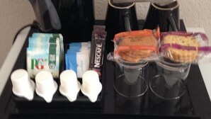 Una bandeja con cafetera, tazas, una caja de Nescafé, pañuelos desechables y algunos aperitivos.