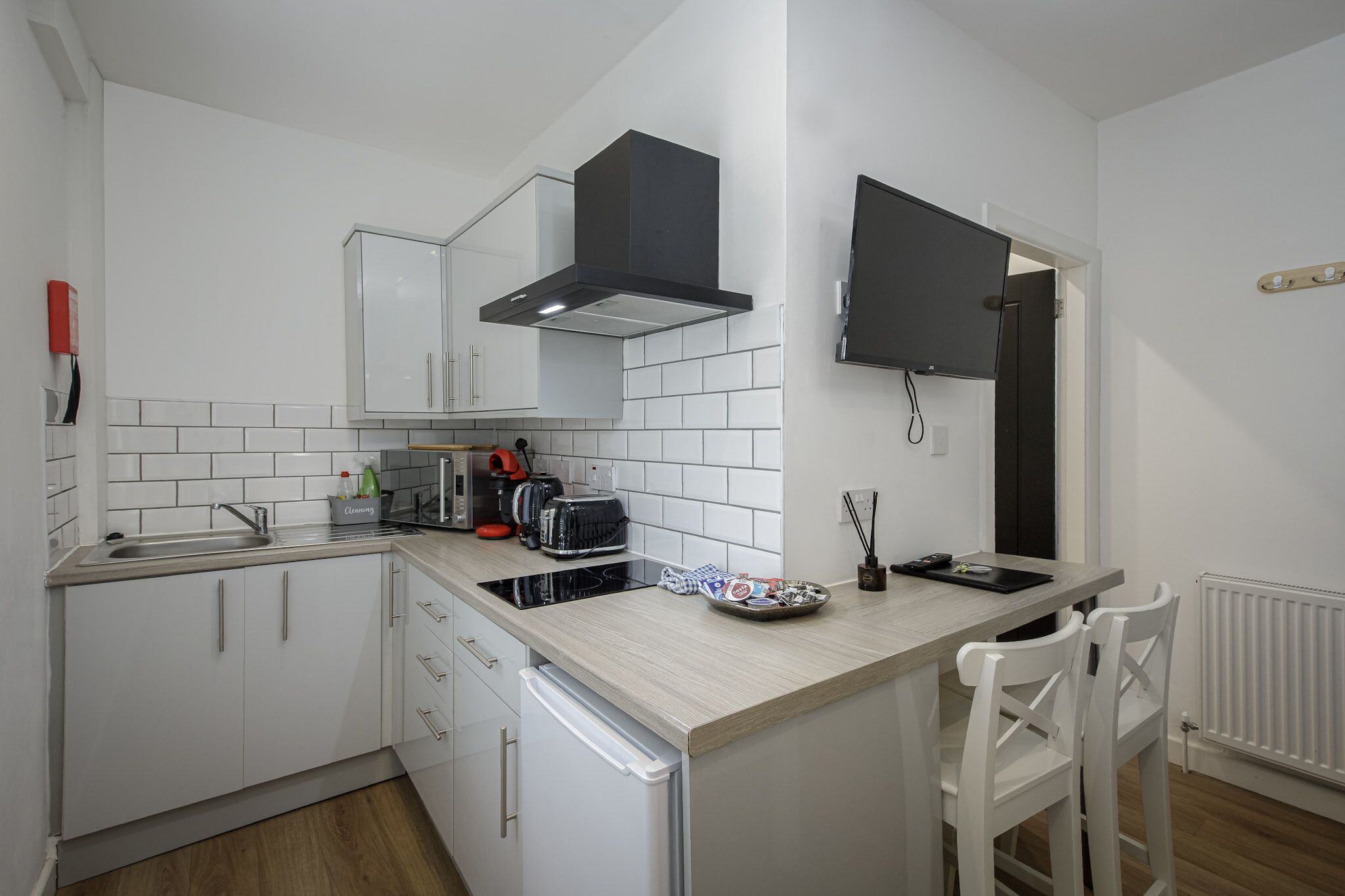 A compact kitchen with white cabinets, a microwave, a coffee maker, and a small dining area with a chair.
