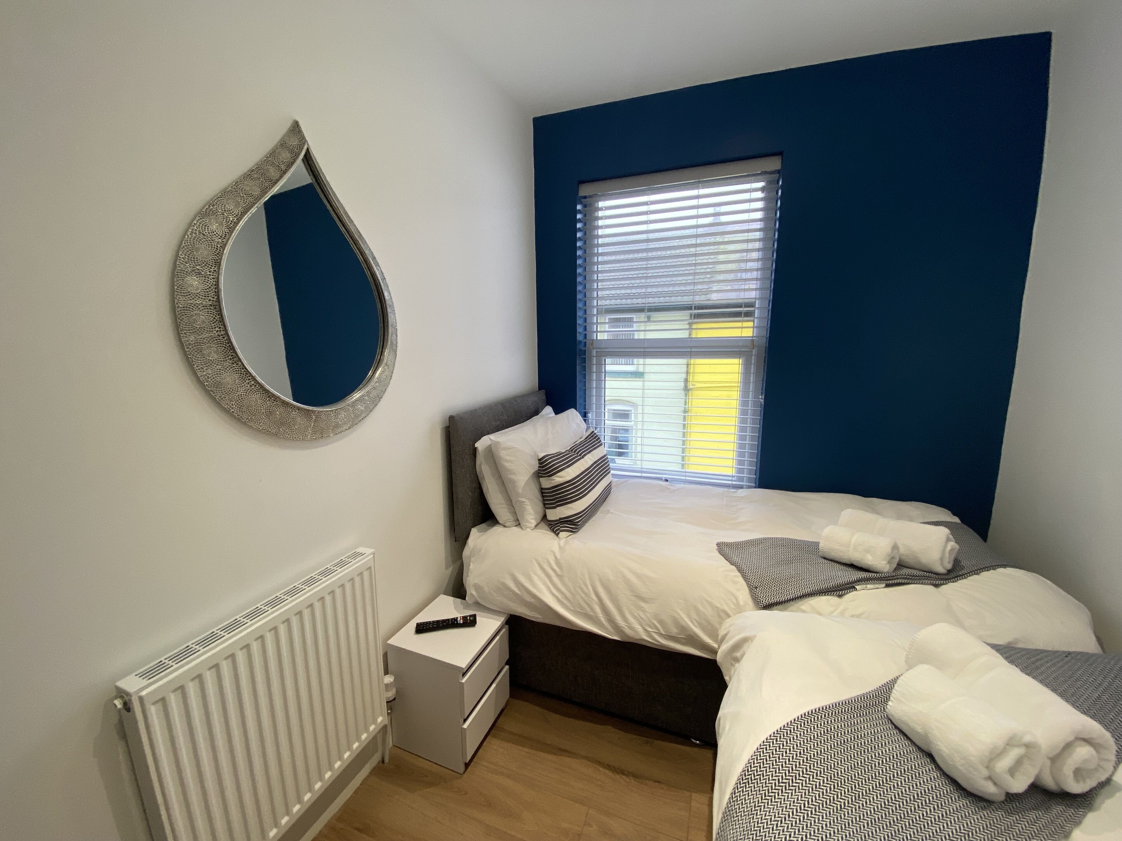 A bedroom with a bed, a bedside table, a mirror, a window, and a radiator.