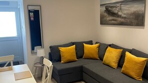 A modern living room with a grey sectional sofa, yellow cushions, a dining table with chairs, and a painting of a boat on the wall. - Blackpool Abode - 20 Bairstow Street (Blackpool)