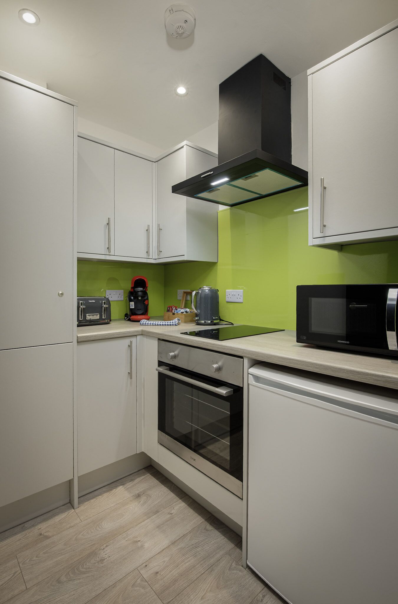 A modern kitchen with white cabinets, a black range hood, a microwave, and a kettle on the counter.