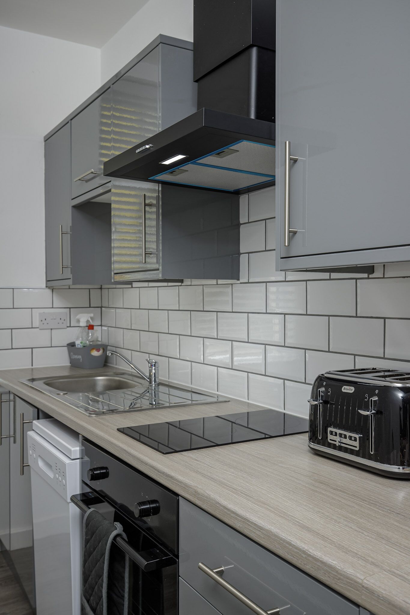 Een moderne keuken met grijze kastjes, een zwarte afzuigkap, een Breville broodrooster en een RVS spoelbak.