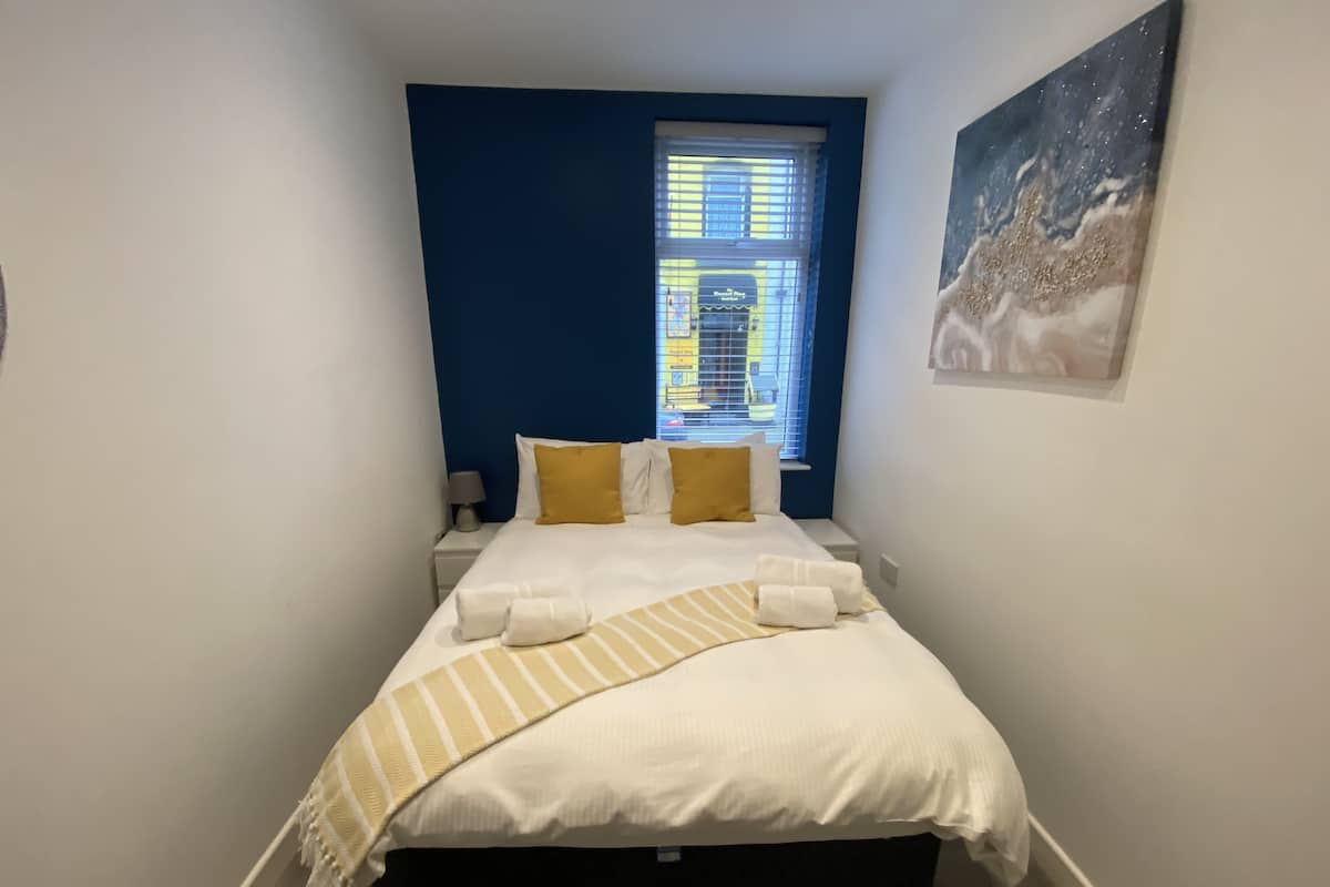 Ein Schlafzimmer mit einem Bett, zwei Nachttischen, einem Fenster mit Jalousien und einem an der Wand hängenden Kunstwerk.