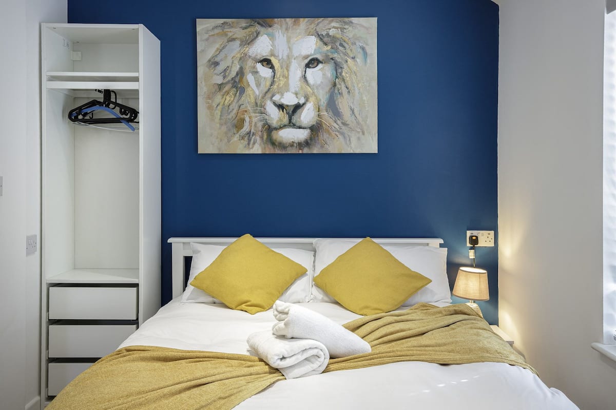 Ein Schlafzimmer mit Bett, zwei Kissen, einer Decke, einem Löwenbild, einem Kleiderschrank und einem Nachttisch mit Lampe.