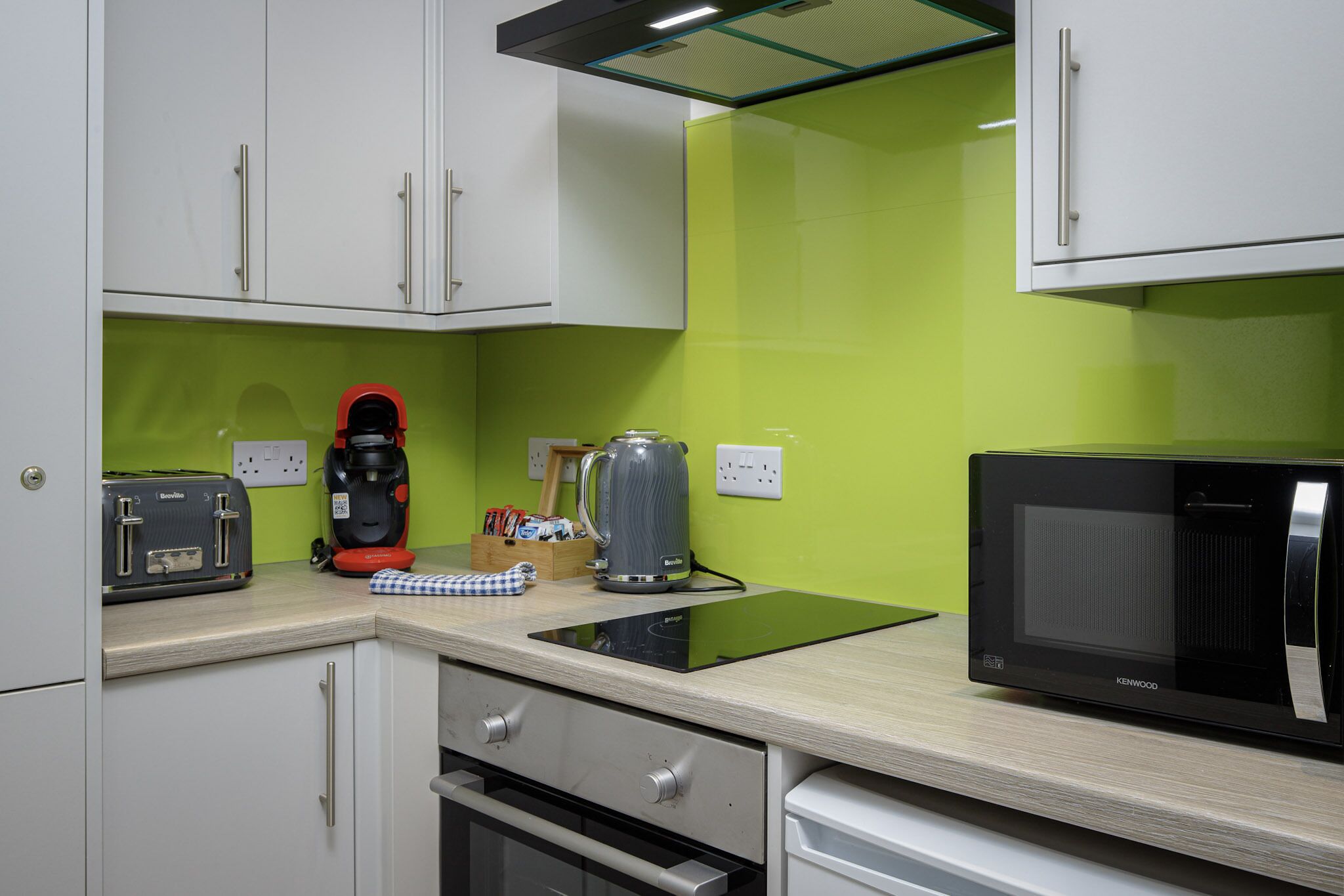 A compact kitchen with white cabinets, a black microwave, a kettle, and a toaster.